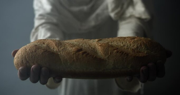 Jesus Christ in white robe and glowing light holding bread and offering it as a representation of the gospel and Jesus as the bread of life in cinematic, dramatic slow motion.
