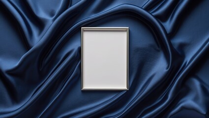Metal frame on dark blue satin fabric. Rectangular silver border and blank white space. Elegant folded textile background with smooth shiny surface.