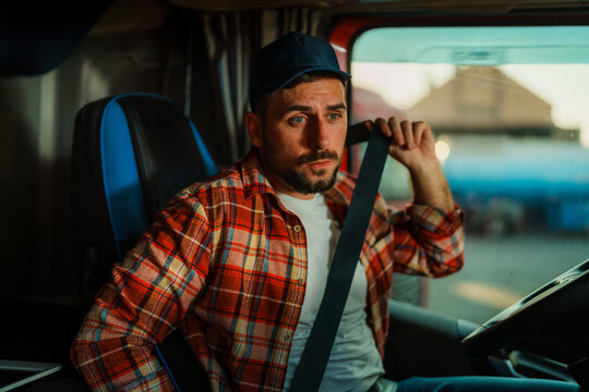 A professional truck driver with a heat and in plaid shirt fastening seat belt before starting a new trip.