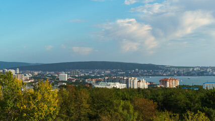 Fototapeta premium Panoramic cityscape with modern buildings, lush greenery, and serene waterfront under partly cloudy sky of sea resort Gelendzhik.