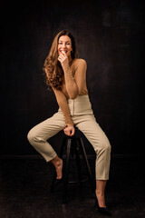 Full length of brunette haired woman sitting against dark background
