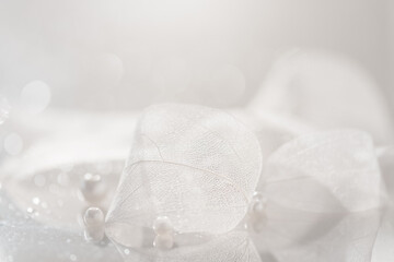 Delicate wedding invitation card with transparent white leaves and pearl beads, abstract art background with skeleton leaves, selective focus