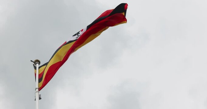 The National Flag of Uganda flutters in the wind. Great for news. Close-up. The Ugandan flag against a blue sky. 4K video.