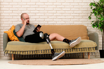 Man amputee with bionic prosthesis leg disability spending time at home, sitting on the sofa and...