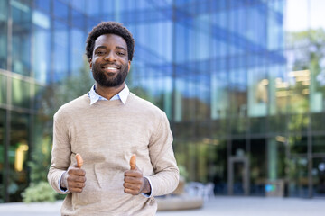 A smiling black man gives a thumbs up, standing in front of a modern building. The scene conveys...