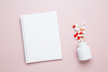 White bottle container with colorful medication capsules and blank notebook. Concept of medicine,...