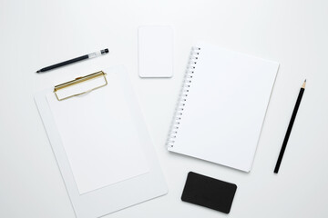 On a white background, an empty mock up notebook and clipboard, white and black cards, monochrome stationery items arranged neatly