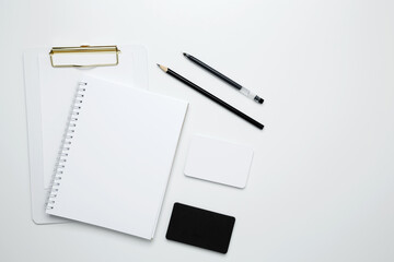 On a white background, an empty mock up notebook and clipboard, white and black cards, monochrome stationery items arranged neatly