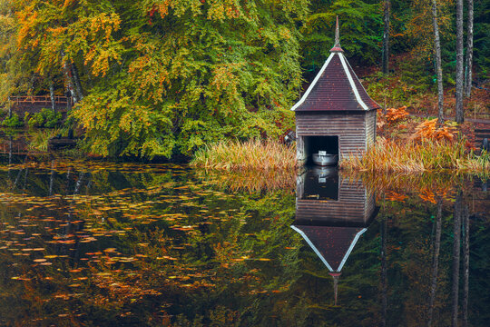 Scenic Autumn View of Loch Faskally, Pitlochry, Scotland, Featuring a Quaint Wooden Boathouse, Still Water with Floating Leaves, and Surrounding Trees in Full Seasonal Colour