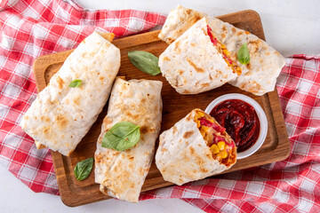 Homemade oven baked Pizza Burritos, pizza style quesadilla wraps with pepperoni or salami, tomatoes, cheese and corn, on kitchen table with hot tomato sauce, copy space