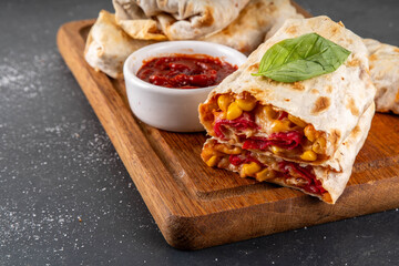 Homemade oven baked Pizza Burritos, pizza style quesadilla wraps with pepperoni or salami, tomatoes, cheese and corn, on kitchen table with hot tomato sauce, copy space