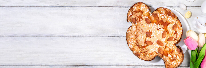 Italian Easter Colomba Cake, Colomba di Pasqua, sweet sugared dove-shaped sponge cake with glazed nuts and fruits, festive fruit- stuffed bread on white Easter holiday decorated table copy space