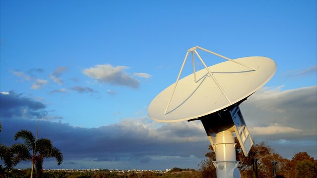 Large parabolic antenna for telecommunications, used for receiving and transmitting data, standing tall against a backdrop of blue sky and clouds, highlighting its role in global communication