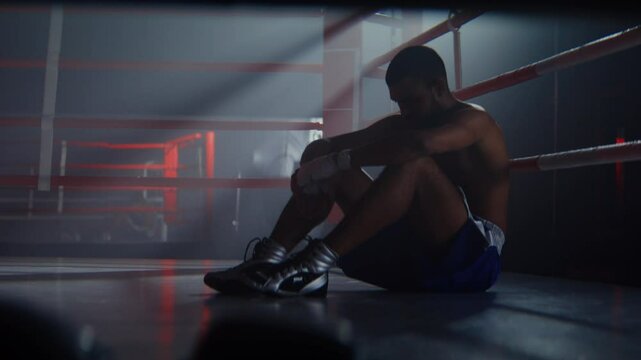 Upset African American boxer sits on ring after fight losing