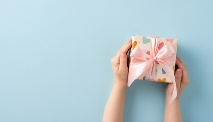 Gift box with a decorative pink ribbon held in hands against a minimalist background expressing...