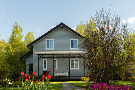 Contemporary wooden house have nice landscaping, with shrubs, green lawn and spring flowers. Traditional russian dacha in Moscow region. Outdoors. Backyard and traditional relax gardening.
