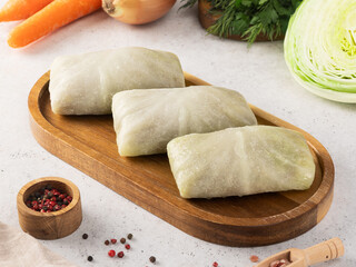 Frozen cabbage rolls and minced meat lie on a wooden board against a background of cabbage, carrots and onions.