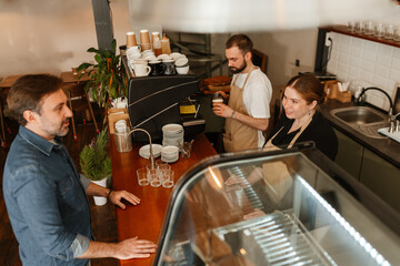 A female barista smiles as she takes a customer's order while her coworker prepares coffee. A concept of service, effective communication with customers, and the dynamics of working life.
