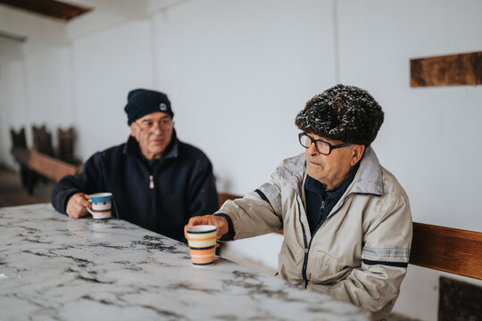 Two senior men sitting at a table while having coffee together, creating a feeling of companionship. They appear relaxed and engaged in conversation.