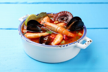Delicious seafood soup in bowl on blue wooden table, closeup