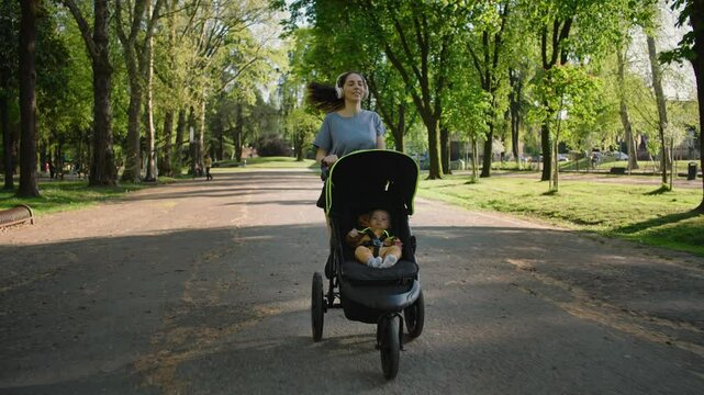 A young sporty woman runs in the park with her son in the running board. Mom is happy to do sports in the park with her newborn baby on a sunny day. Concept of power, fitness, family