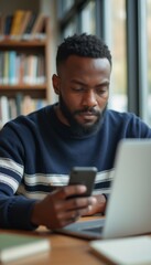 Fototapeta premium A thoughtful Black man is engrossed in his smartphone while seated at a wooden table in a warm, inviting library. The scene captures a blend of modern technology and a love for learning, showcasing