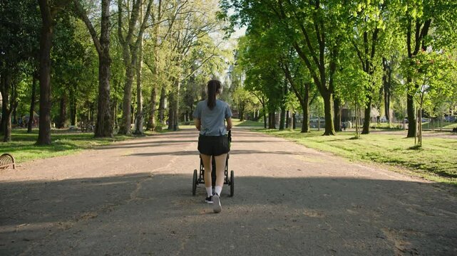 A young sporty woman walks in the park with her son in the running board. Mom is happy to do sports in the park with her newborn baby on a sunny day. Concept of power, fitness, family