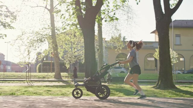 A young sporty woman runs in the park with her son in the running board. Mom is happy to do sports in the park with her newborn baby on a sunny day. Concept of power, fitness, family
