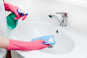 Person Cleaning Bathroom Sink With Spray And Sponge