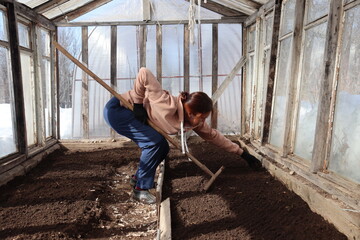 woman works in a greenhouse preparing soil for planting using rake.
