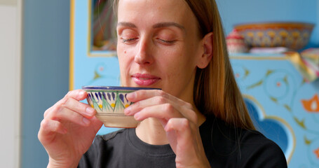 Woman drinks green tea from a traditional bowl in cozy Uzbek interior