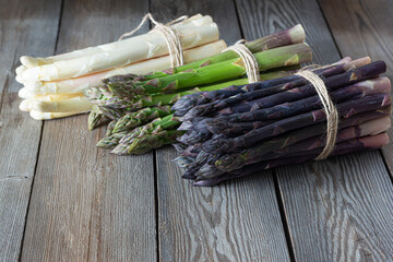 Raw white, purple, green asparagus on wooden background. Healthy food concept, place for copy...