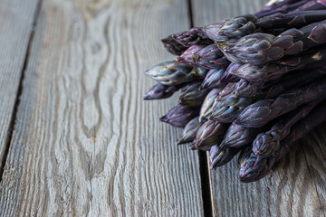 Fresh bunch of purple asparagus on dark wooden background. Healthy food concept. The vegetable is rich in fiber, a natural prebiotic.