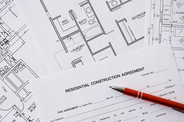 Pen on residential construction agreement and planning blueprints of residential building project