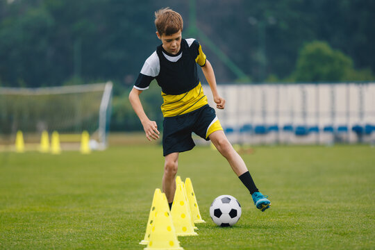 Young Football Player Dribbling Ball Around Training Cones. Soccer Practice For Youth. Soccer Training Facility For Teenage Soccer Team - Powered by Adobe