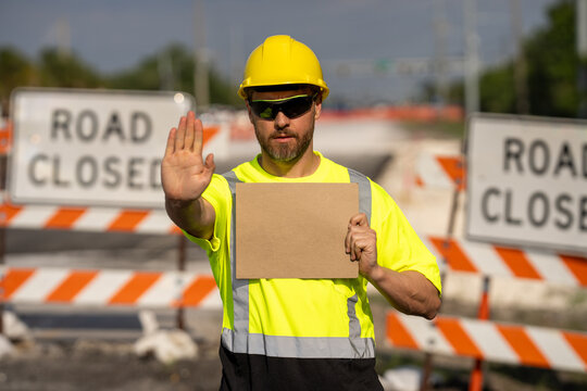 No trespassing. Construction worker with outstretched hand showing stop gesture warning. Stop sign in hands of worker. Concept he warns of danger. An engineer holds up an empty billboard near roadwork