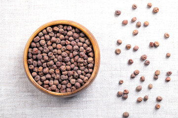 Snow pea seeds in a wooden bowl on linen. Seeds of the snow pea plant, an edible-pod pea, also known as Chinese pea pods. Dried, brown, mature fruits for future planting or sprouting as microgreens. 