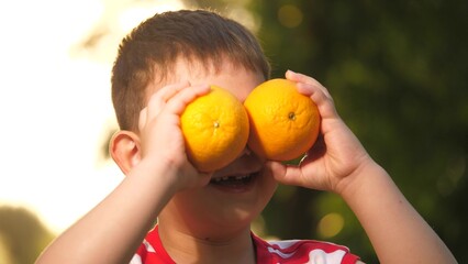 Small child holds oranges in eyes area having weekend outdoors. Happy boy holds oranges pretending...