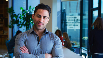 Obraz premium Portrait Of Mature Businessman Standing In Busy Modern Office With Colleagues In Background