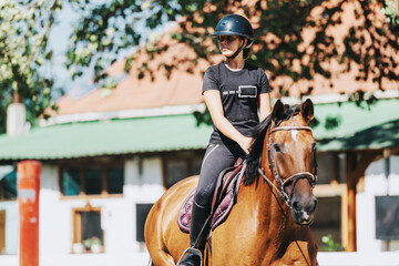 A young female equestrian rides her horse confidently in an outdoor setting. The sunny day and serene environment highlight her passion for horseback riding and equestrian sports.