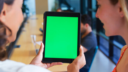 Close Up Of Two Businesswomen Looking At Digital Tablet With Green Screen In Shared Office