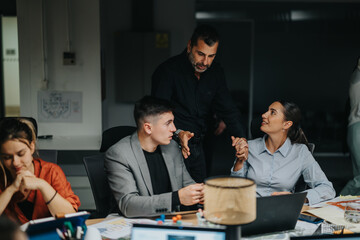A group of diverse coworkers in an office setting discusses projects and brainstorms ideas. They appear focused while collaborating and working late into the night, emphasizing teamwork and innovation