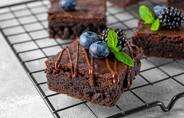 Chocolate brownies squares with chocolate glaze and fresh berries on top on a baking rack on a gray...