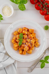 Traditional potato gnocchi with tomato sauce, parmesan cheese and fresh basil on a plate on a white wooden background. Italian cuisine. Top view, copy space.