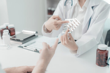 Young Asian man consulting with female doctor in medical office, discussing health problems and explaining. Doctor and patient are sitting together at a table in examination room.