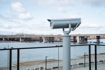 A security camera is mounted high atop a pole, carefully positioned to overlook a flowing river,...
