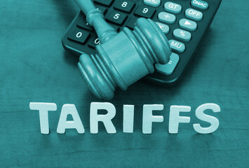 Judge gavel and calculator with word tariffs on wooden table