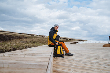 An Adventurous Hiker is Enjoying a Peaceful Moment Relaxing by the Beautiful Shoreline, Dressed in...