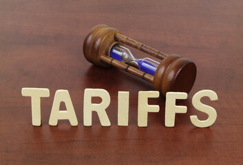 Word tariffs and hourglass on table close-up. Delay of tariffication concept.