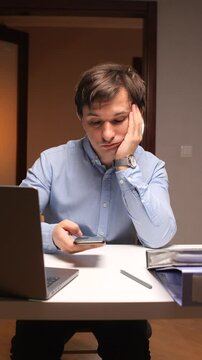 vertical video Bored office worker browsing smartphone at desk